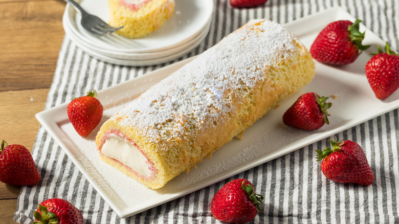 homemade arctic roll on white dish with fresh strawberries