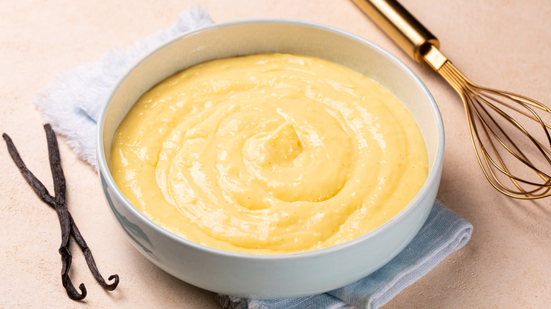 A bowl of custard next to a whisk and vanilla beans