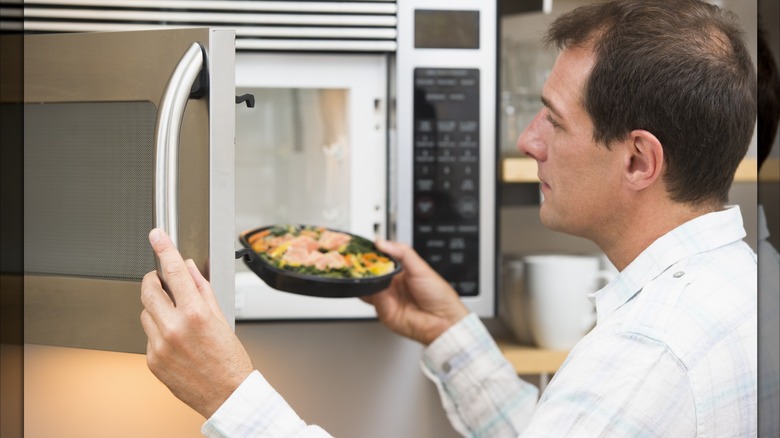 A man putting a bowl of salmon and vegetables in a microwave.