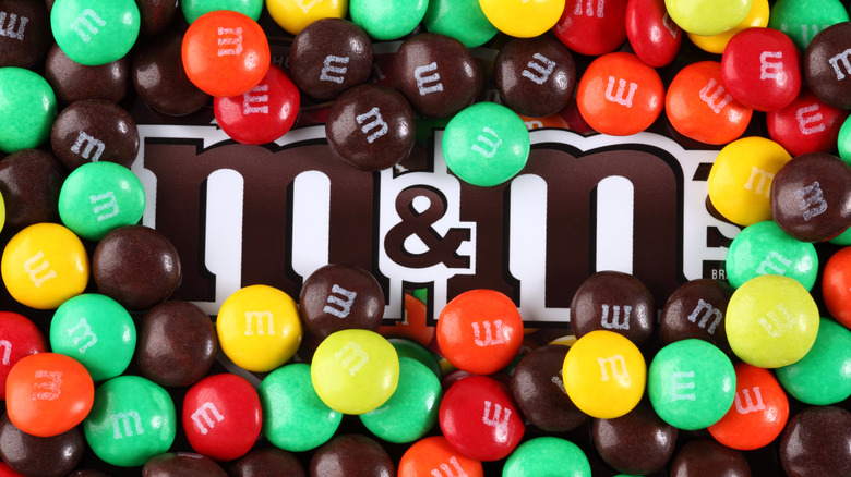 A bag of M&M's surrounded by individual M&M's