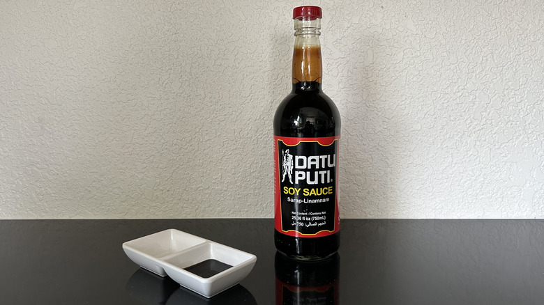A large bottle of Datu Puti soy sauce with dipping dish nearby