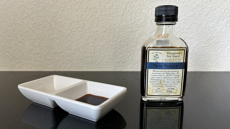 A small bottle of Bluegrass soy sauce next to sauce dish
