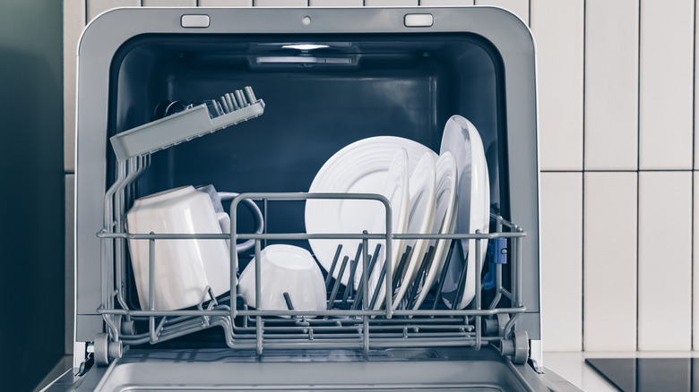 Compact portable dishwasher on countertop open with a few dishes inside