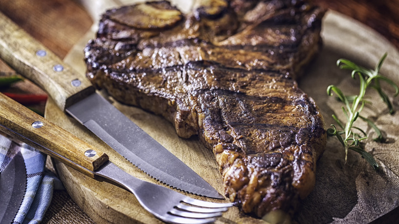 grilled Porterhouse steak on wood board with fork and knife