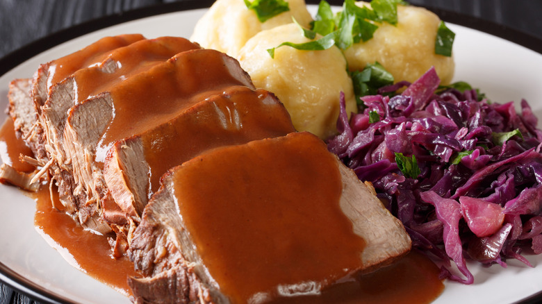 A plate of sauerbraten with gravy, red cabbage, and potato dumplings