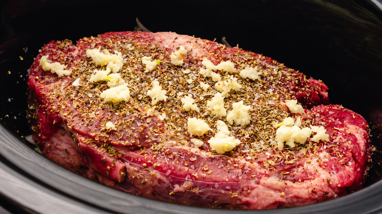 Pot roast in a slow cooker, topped with minced garlic and herbs