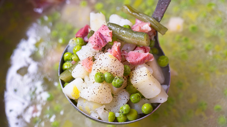 chunks of ham, potatoes, peas, and green beans in soup ladle