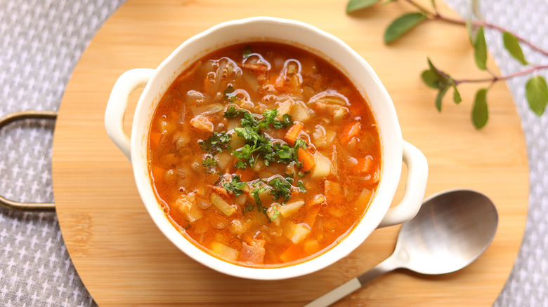 White bowl with handles full of bean and potato stew on top of round wooden board with spoon