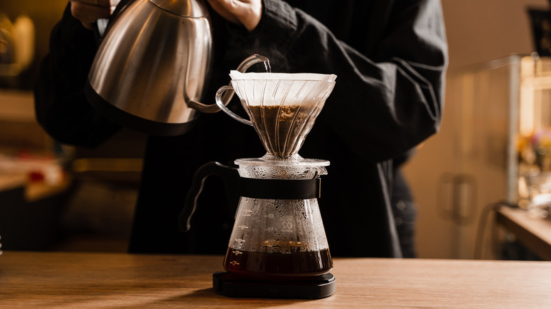 Person making pour over coffee with a stainless steel gooseneck kettle.