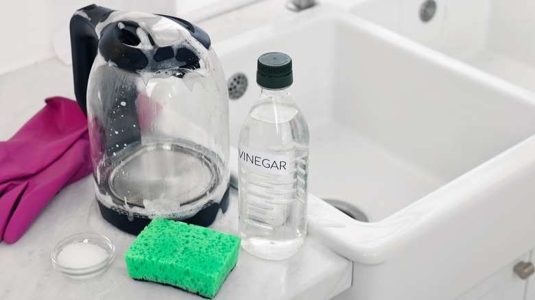 A bottle of vinegar next to a sink with a green sponge