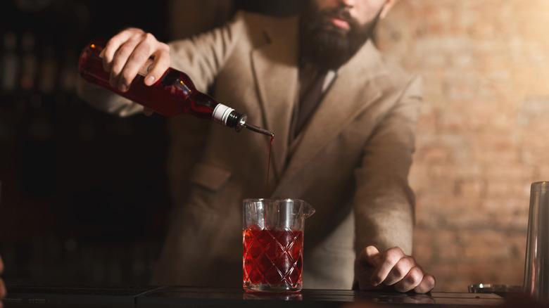bearded bartender pours grenadine syrup into cocktail mixing glass