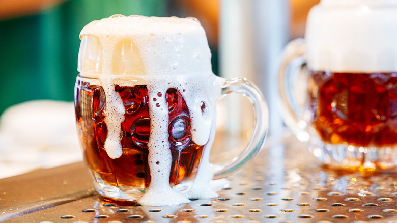 Old-fashioned mug of beer with foam flowing over the top.