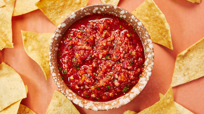 A bowl of red salsa surrounded tortilla chips