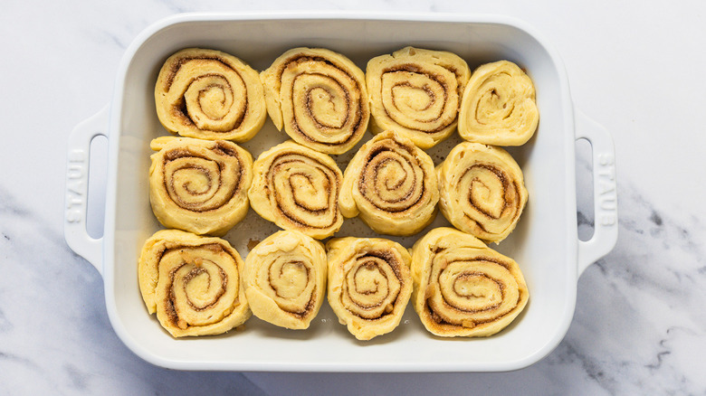 Raw cinnamon buns in white dish.