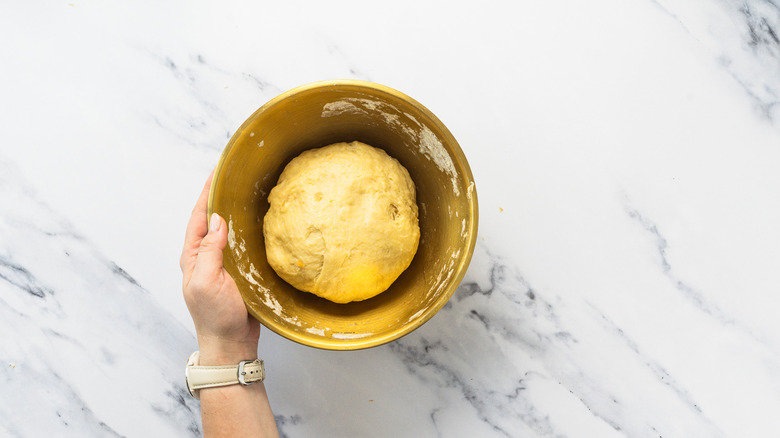 Hand holding bowl with cinnamon bun dough.