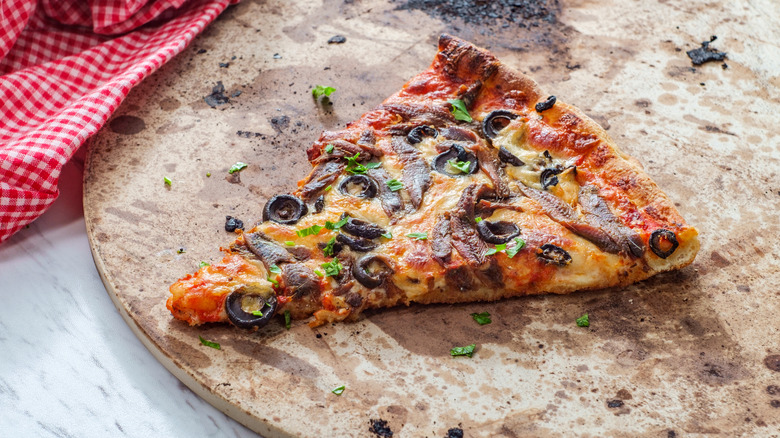 A slice of pizza on a well-used stone.