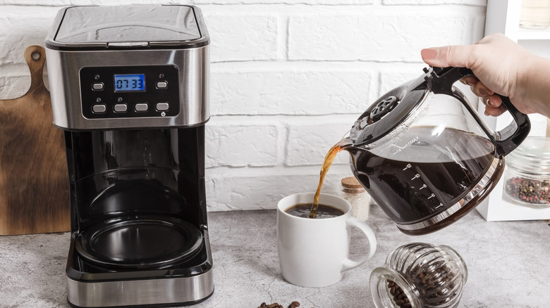 Person pouring coffee from drip machine into cup