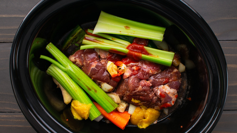 A slow cooker with uncooked meat and vegetables