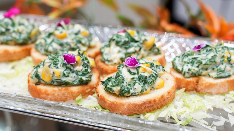 Spinach artichoke crostini garnished with purple flowers on silver tray