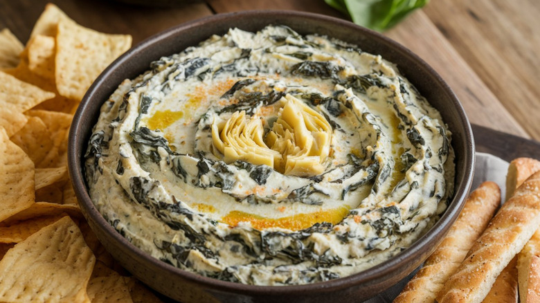 Brown bowl full of spinach artichoke dip garnished with artichoke heart and olive oil