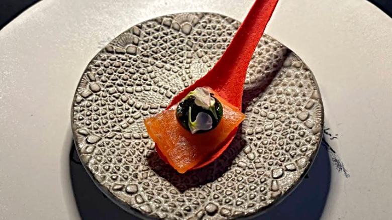 Minimalist dish on a red spoon plated on a decorative plate at Christopher's at Wrigley Mansion