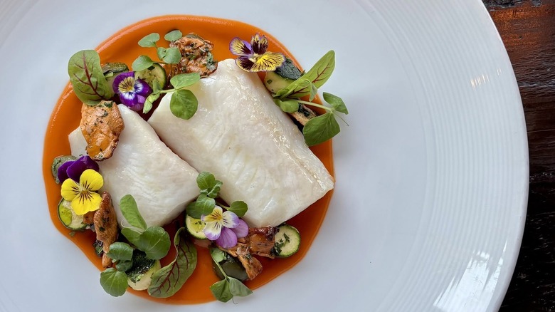 Sablefish over a tomato nage with zucchini, chanterelle, and olive on a white plate at Vida