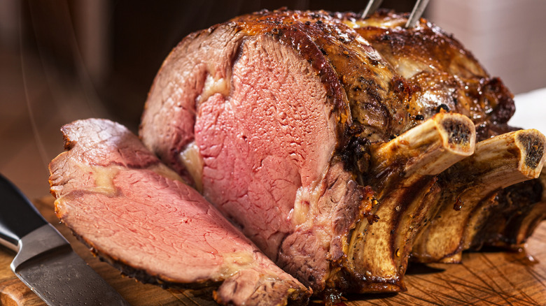 A prime rib roast on a cutting board, sliced into it showing pink medium rare inside