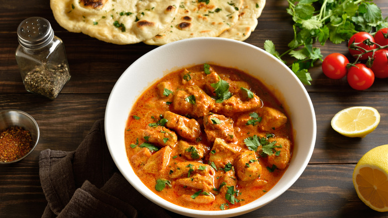 Chicken tikka masala served in a bowl alongside pita bread, lemon, cilantro, and tomatoes.
