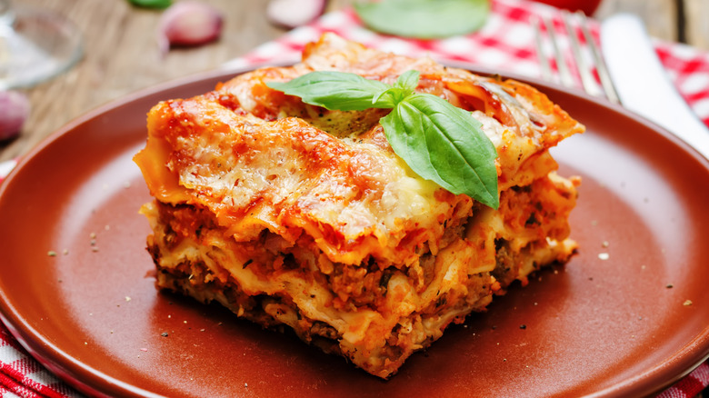 A square slice of lasagna served on a red plate, garnished with basil.