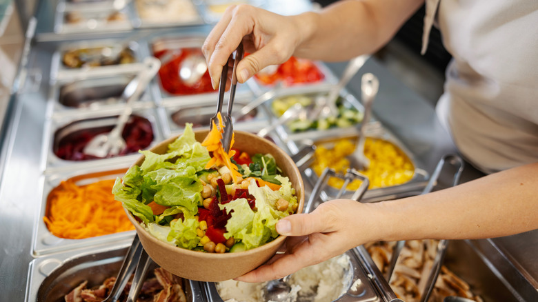 Person using tongs to serve themselves salad from a salad bar.