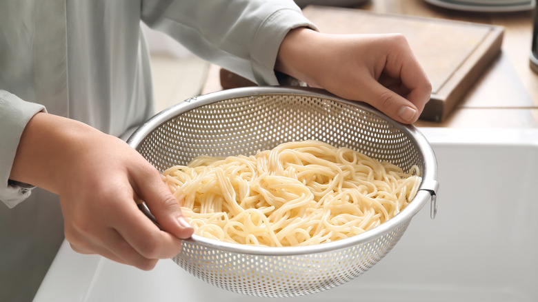 woman holds colander of pasta over sink
