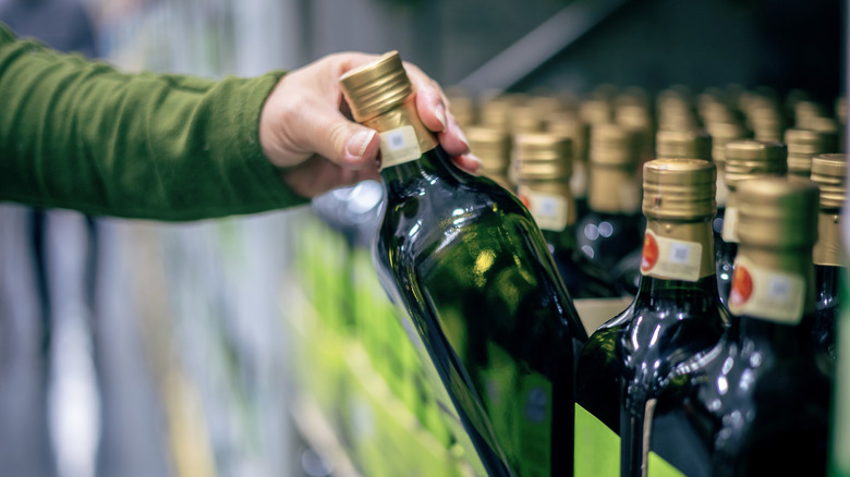 A shopper picking a bottle of olive oil from a store shelf.