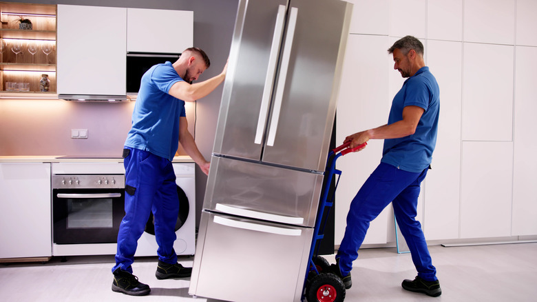 Delivery men rolling a refrigerator on a dolly in a kitchen