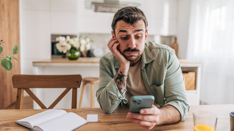 Flustered man waiting in kitchen looking at his phone