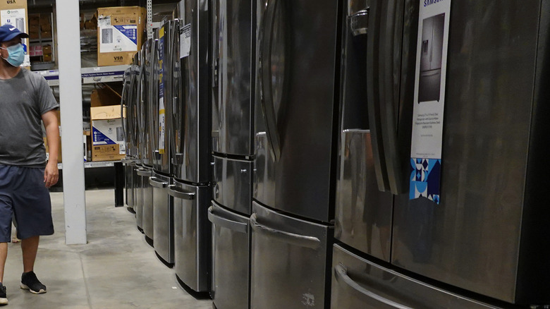 Masked man walking by refrigerators in warehouse store