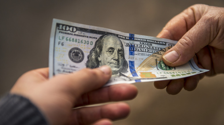 Hand giving $100 to another hand