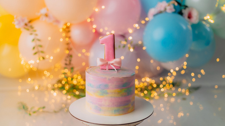 A birthday cake for a one-year-old with birthday decor in the background.