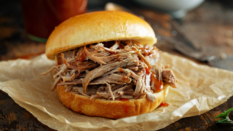 A barbecue pulled pork sandwich sitting on brown paper on a wooden table.