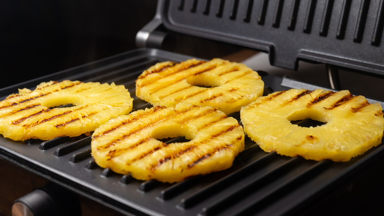 Four pineapple rings already partially grilled on top, sitting on a grill.