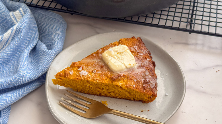 Slice of pumpkin cornbread with butter on plate