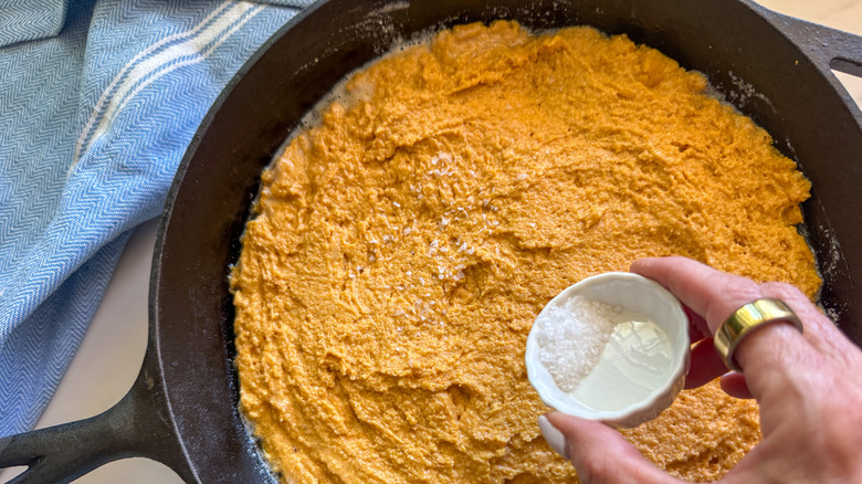 Small bowl of salt pouring over pumpkin cornbread batter
