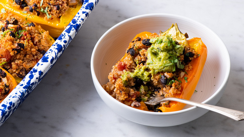 Quinoa stuffed bell pepper with guacamole in a white bowl.