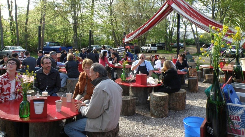 People at red tables sitting on tree stumps outside