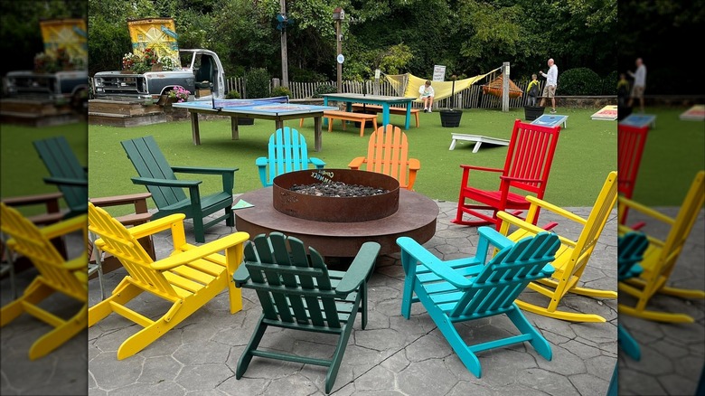 Colorful chairs around a fire pit, with games, hammocks, and an old truck in the background