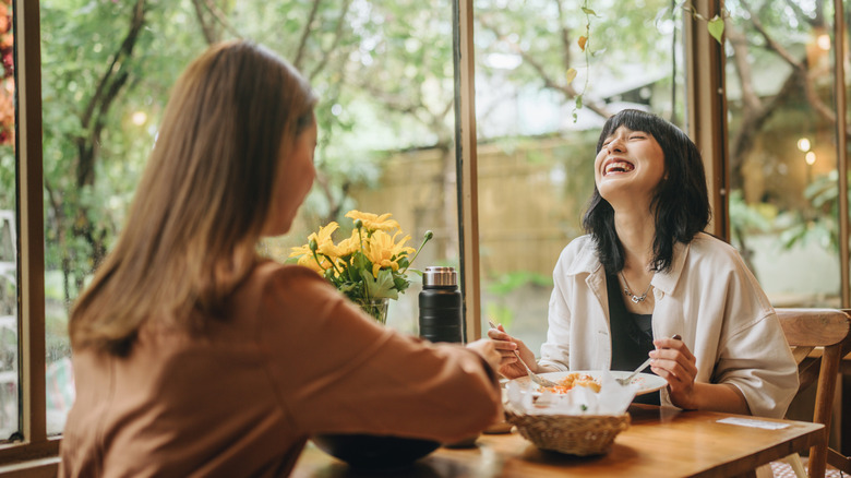 Two people eating food in a restaurant and laughing