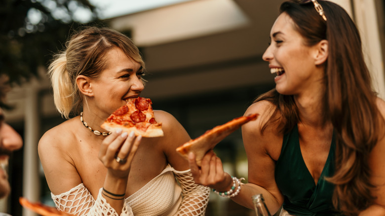 Two friends eating pizza and laughing