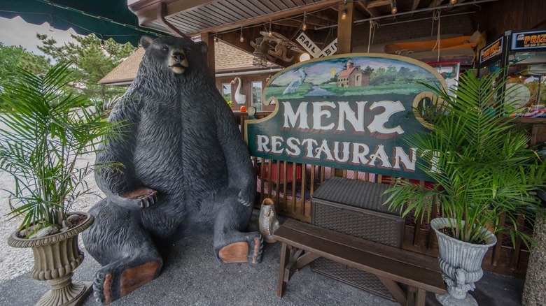 Sign for Menz Restaurant with benches, plants, and a giant bear statue