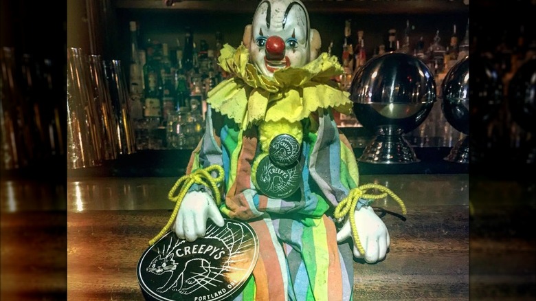 Clown doll sitting on a bar with Creepy's stickers and pins