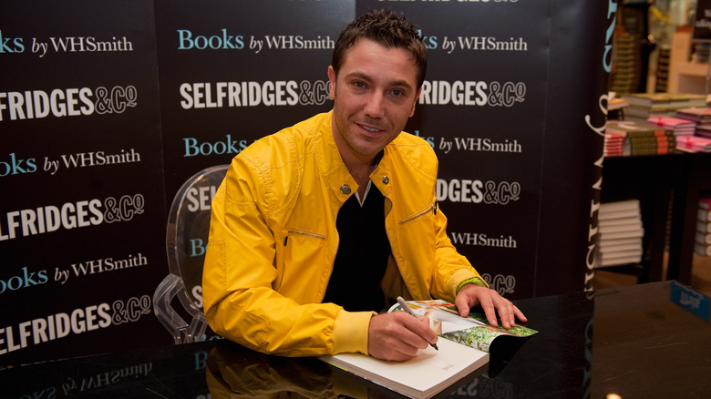 Gino D'Acampo wearing a yellow jacket and signing a book.
