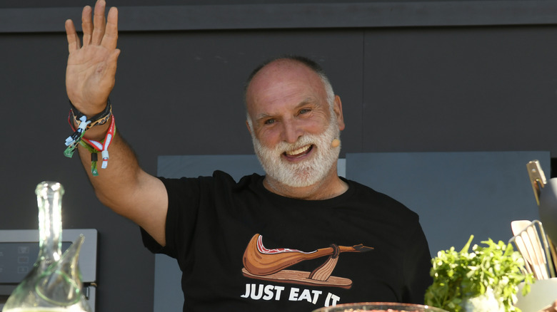 José Andrés smiling, waving with one hand and wearing a black T-shirt that says "just eat it."